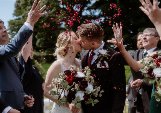 Bride and Groom sharing a Kiss after the ceremony under rose petal confetti